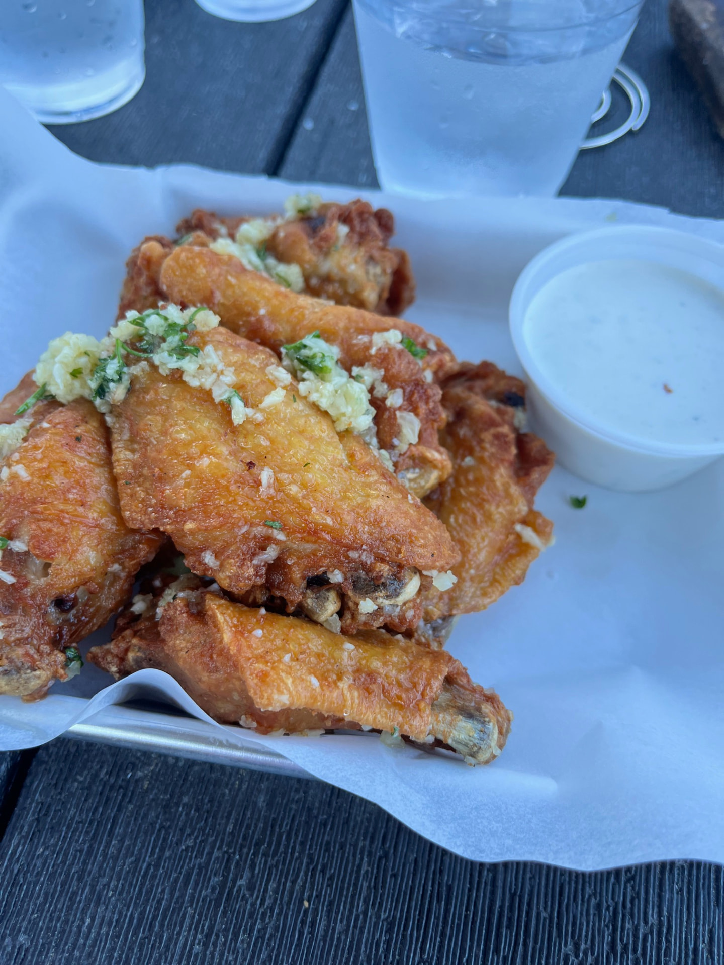 A basket of crispy garlic parmesan wings with a side of ranch on a patio table.