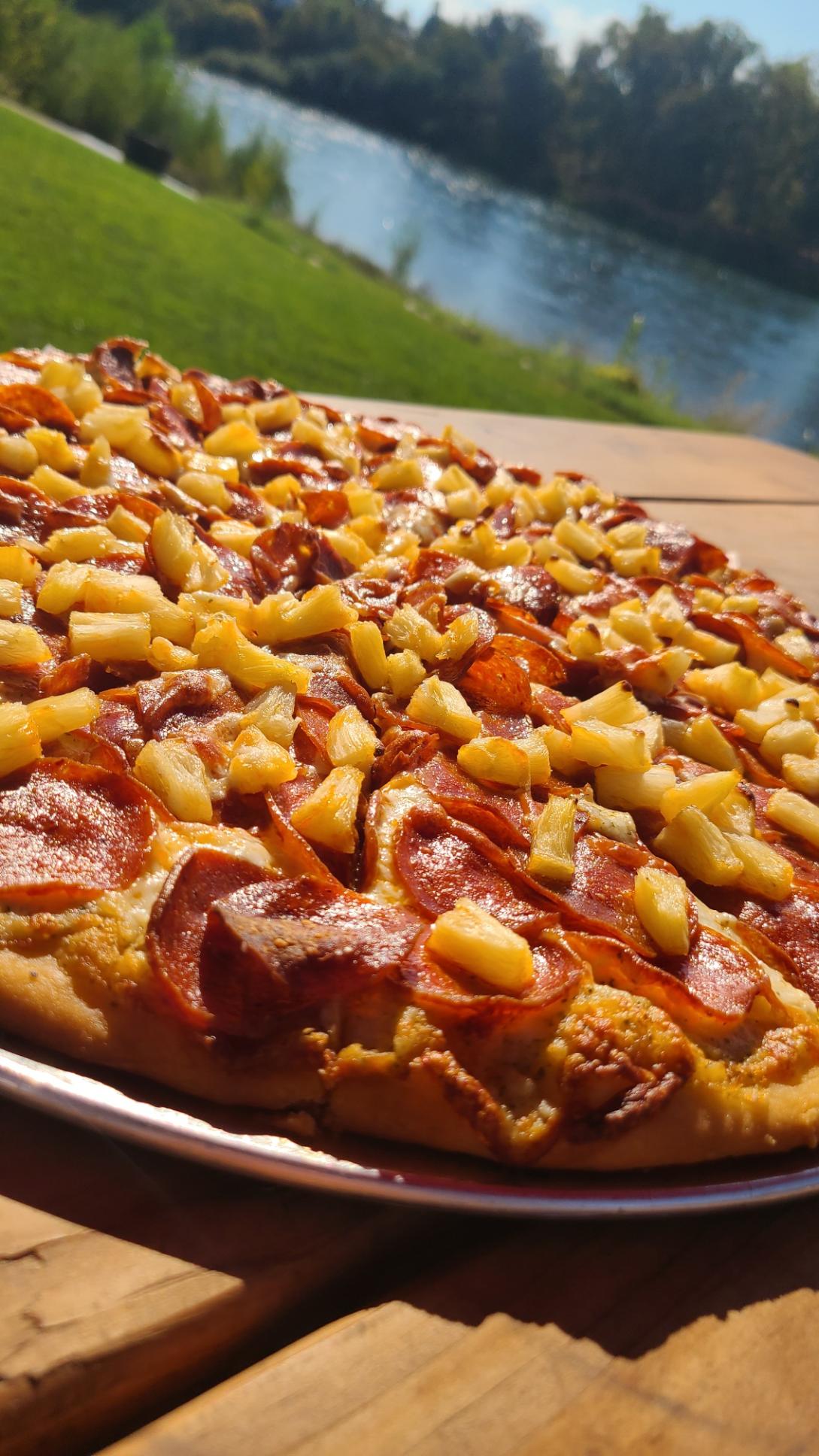 Close-up of a pepperoni and pineapple pizza on a table outdoors at E's Locker Room.